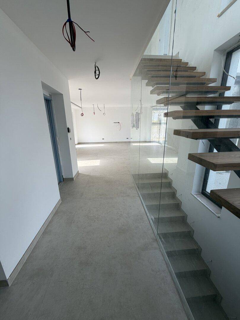 Geräumiger, unfertiger Innenraum mit Fliesenboden und Blick auf die moderne Treppe.