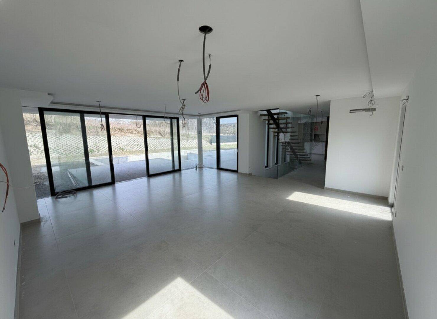 Heller Wohnraum im Bau mit großen Fensterfronten und Blick auf die moderne Treppe.