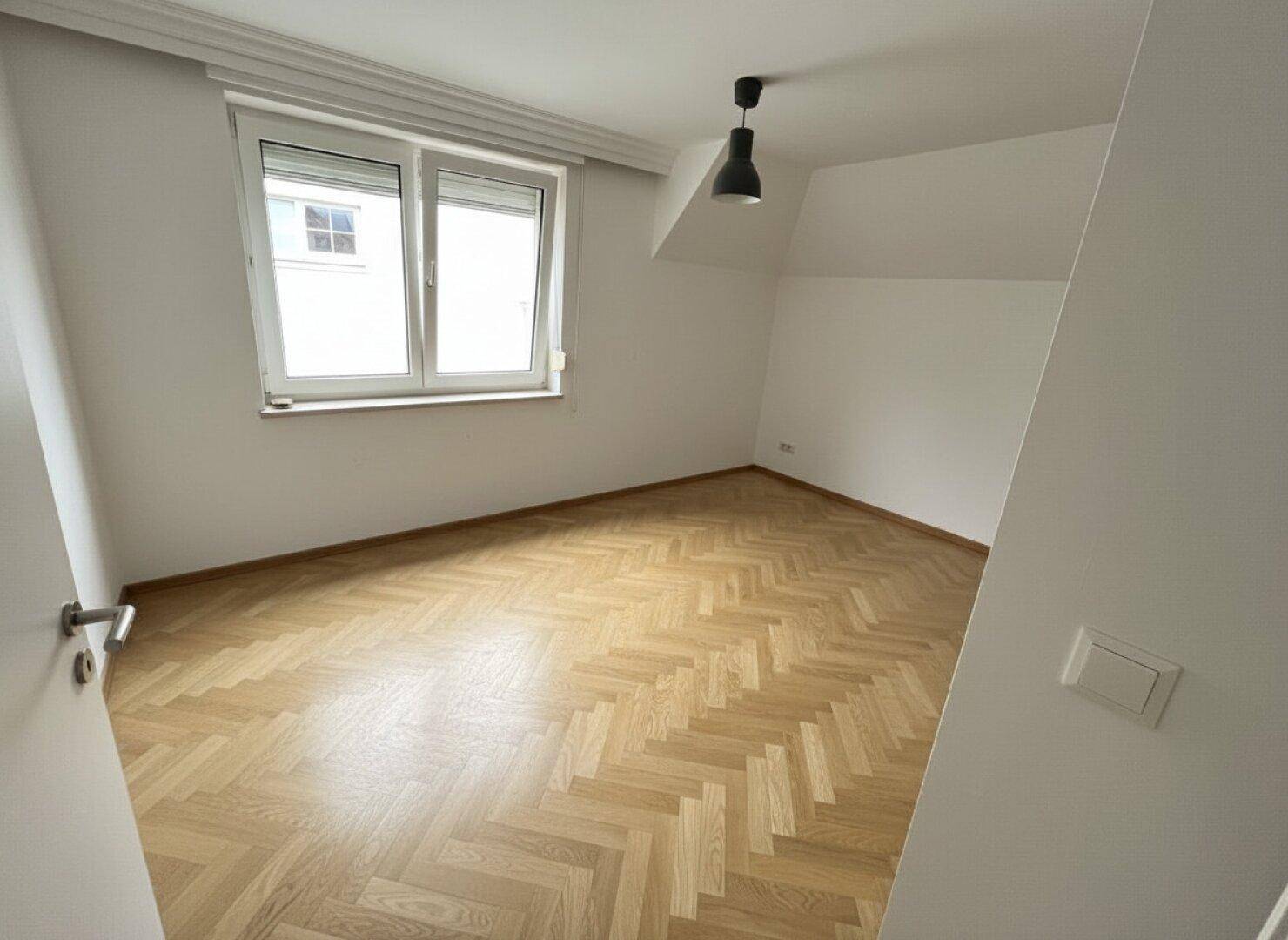 Helles Schlafzimmer mit Fischgrätparkett, weißen Wänden und Dachschräge.