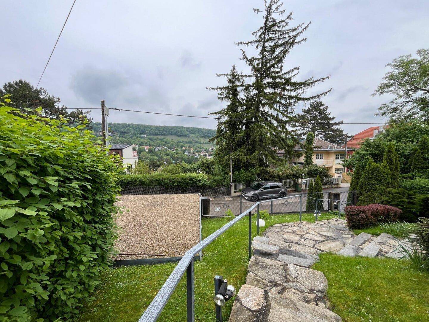 Gepflasterter Weg führt durch den Vorgarten mit Blick auf die grüne Hügellandschaft.