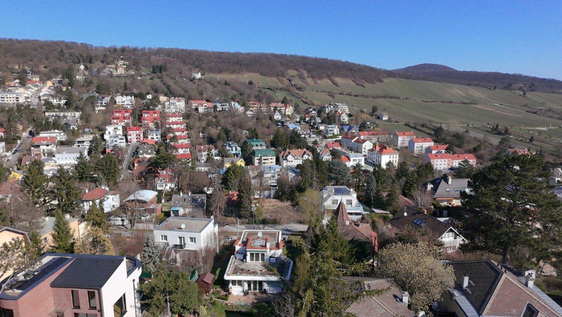 Weitläufige Luftaufnahme der Wohngegend mit vielen Häusern und grünen Hügeln im Hintergrund.