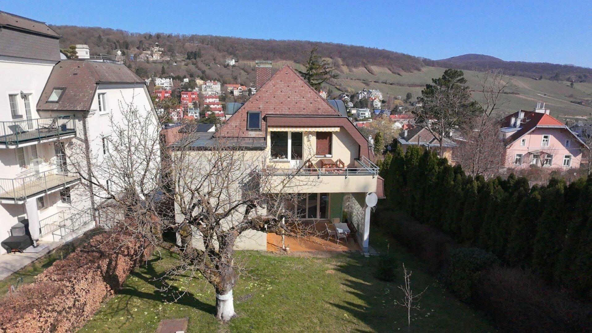 Luftaufnahme des Hauses mit Balkon und Terrasse, umgeben von Bäumen und Hügellandschaft.