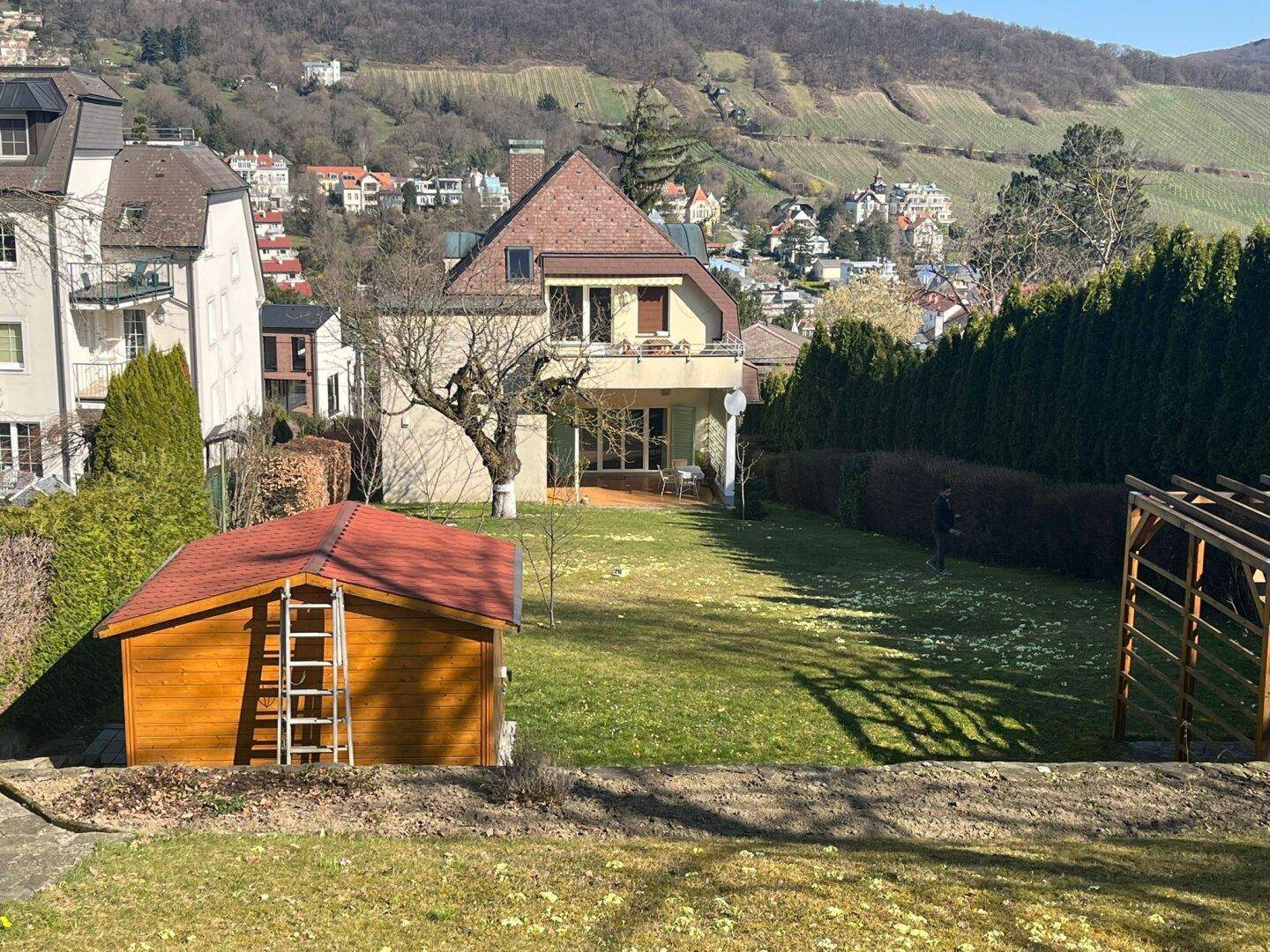 Gepflegter Garten mit Gartenhaus, Rasenfläche und weitem Blick auf die Weinberge.