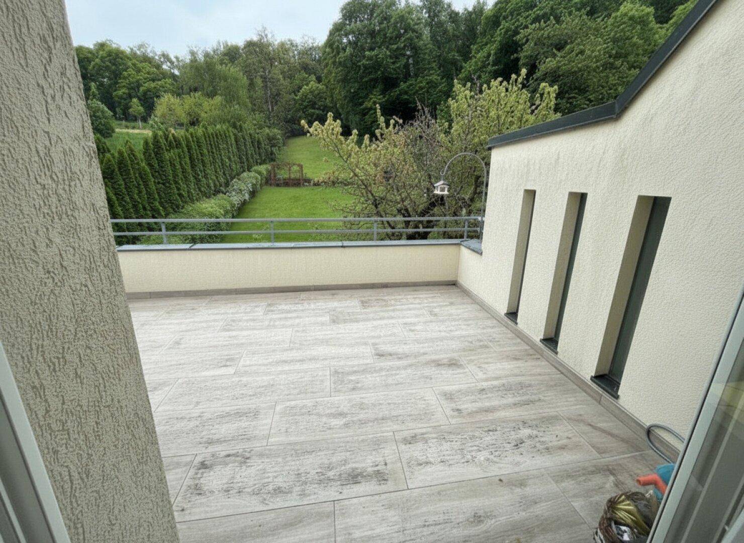 Helle, geflieste Terrasse mit Blick auf den weitläufigen Garten und die umliegende Natur.
