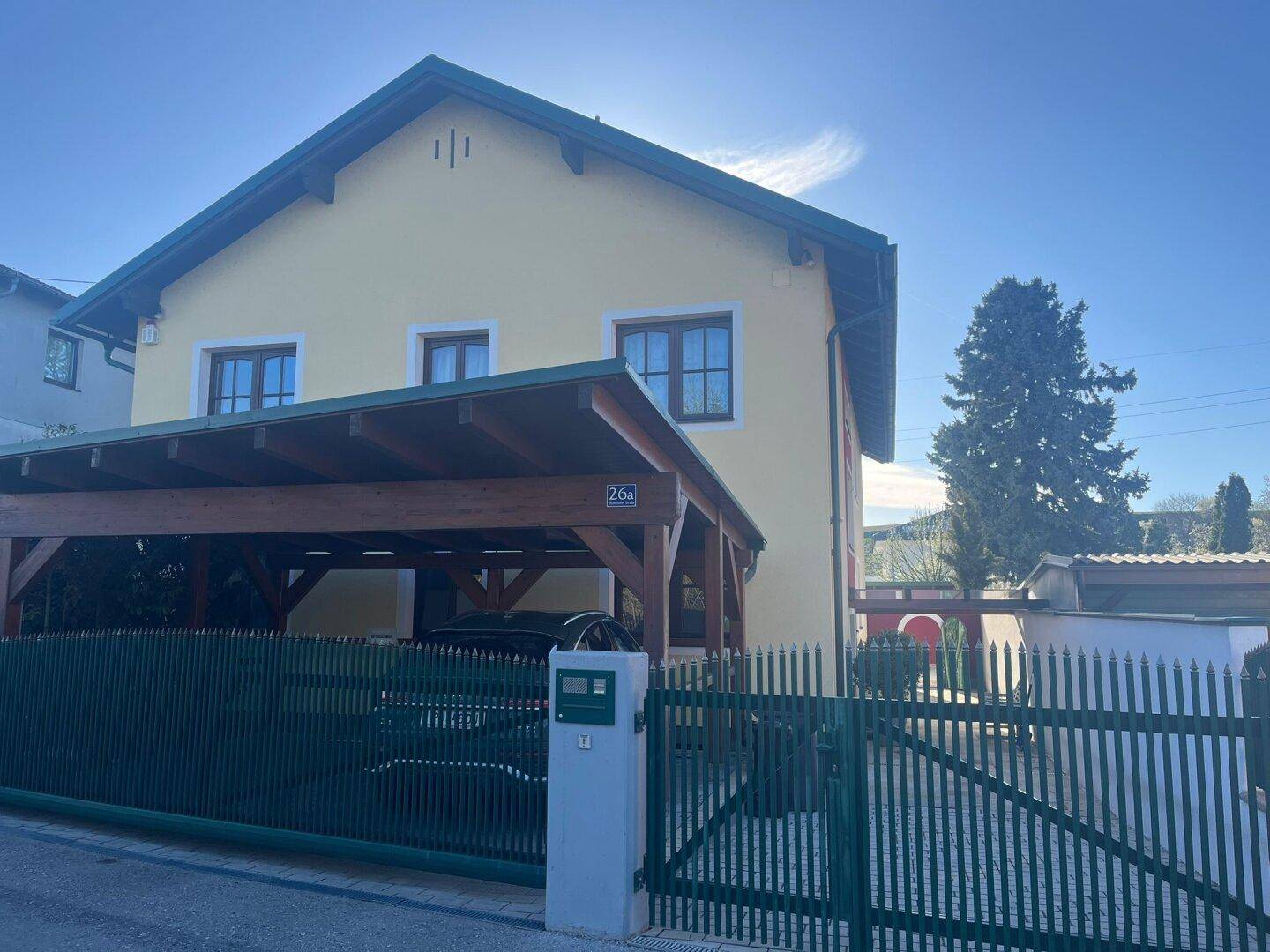 Vorderansicht des Hauses mit Carport und grünem Gartentor unter blauem Himmel.