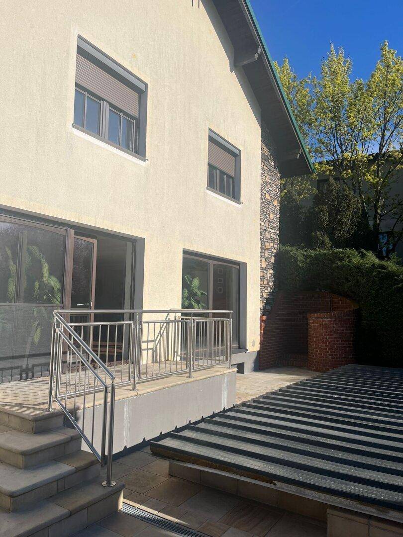 Terrasse mit Edelstahlgeländer und Treppe, die zum Gartenbereich des Hauses führt.