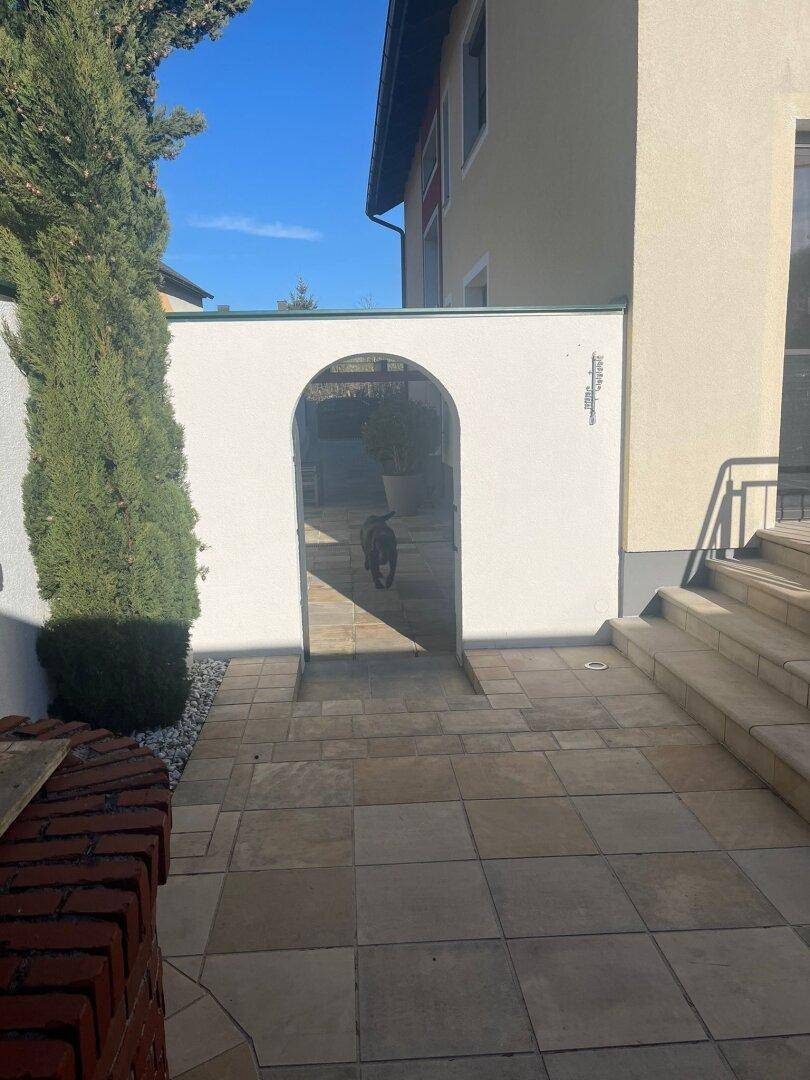 Gepflasterter Weg mit einem dekorativen Torbogen, der zu einem weiteren Bereich führt.