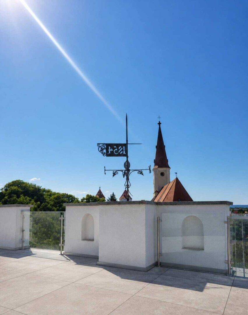 Dachterrasse mit weitem Blick über die Stadt und eine historische Kirche bei Sonnenschein.