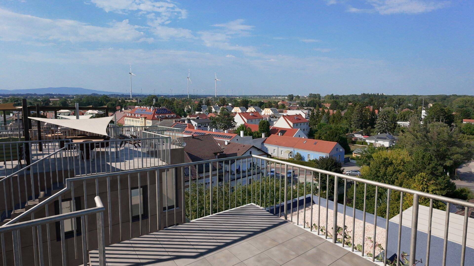 Weitläufige Dachterrasse mit Blick auf die umliegende Stadt und Windräder in der Ferne.