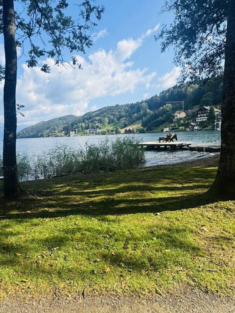 Idyllischer Seeblick mit Bergen im Hintergrund und einem kleinen Steg am Ufer.