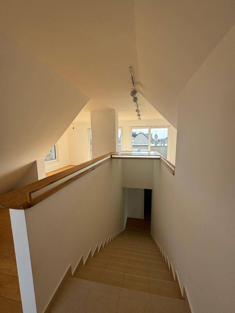 Treppenabgang mit Holzgeländer und Glaspaneelen, führt zu einer unteren Etage mit Holzboden.