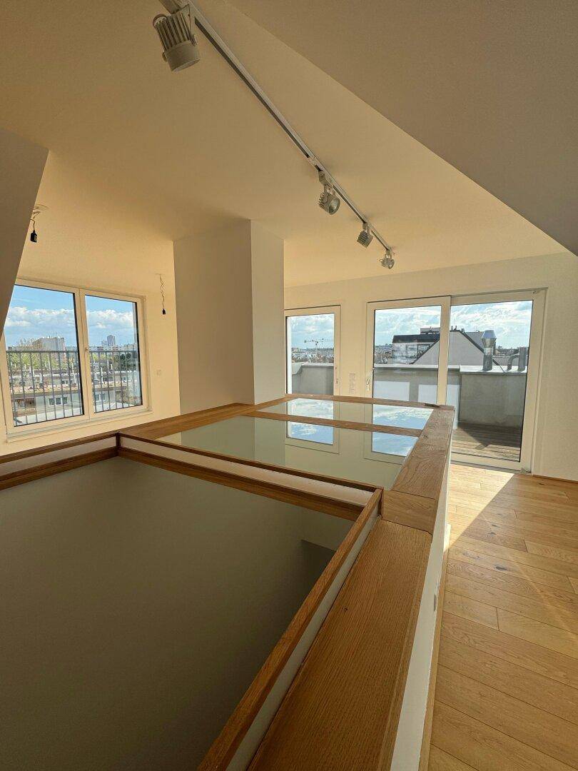 Heller Wohnbereich mit Holzboden, Glasgeländer und Fenstern mit Blick auf die Stadt.