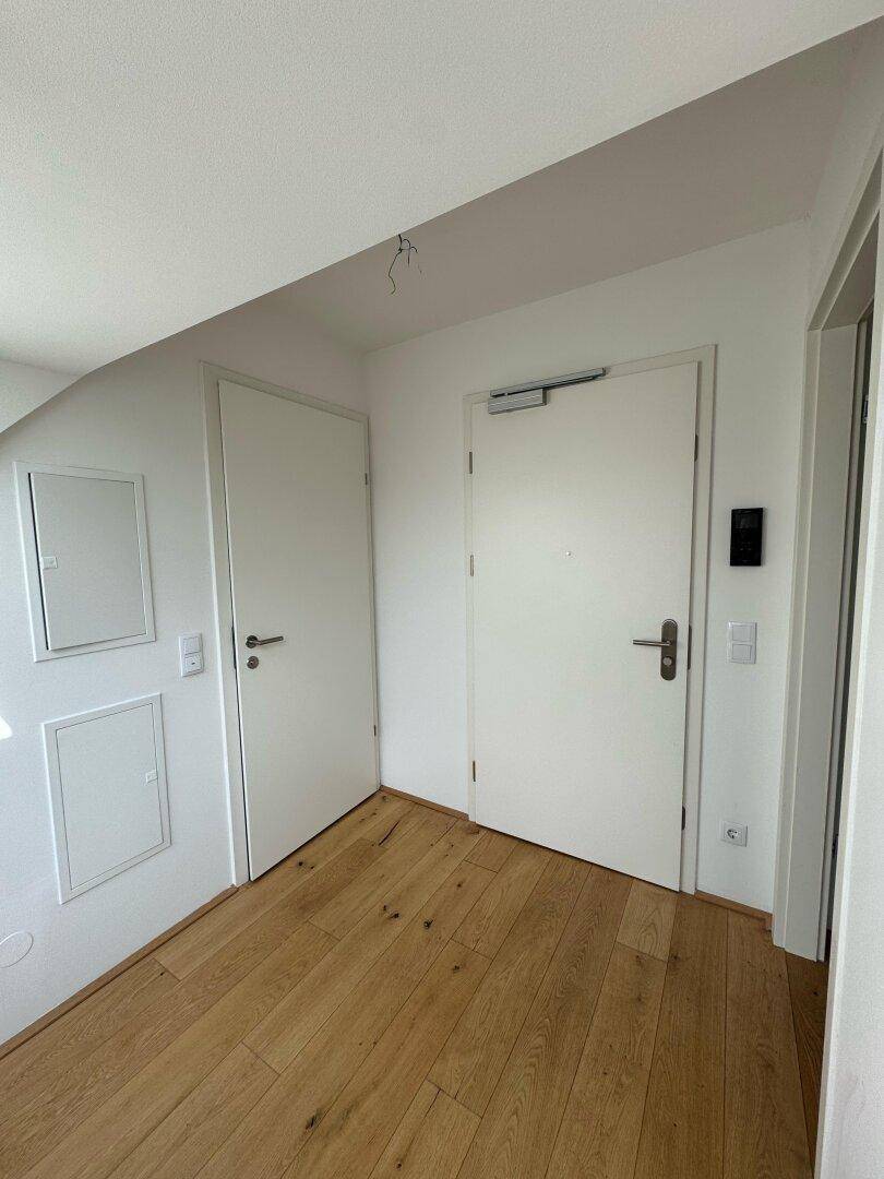 Heller Flur mit Holzboden und weißen Türen, teilweise unter einer Dachschräge gelegen.