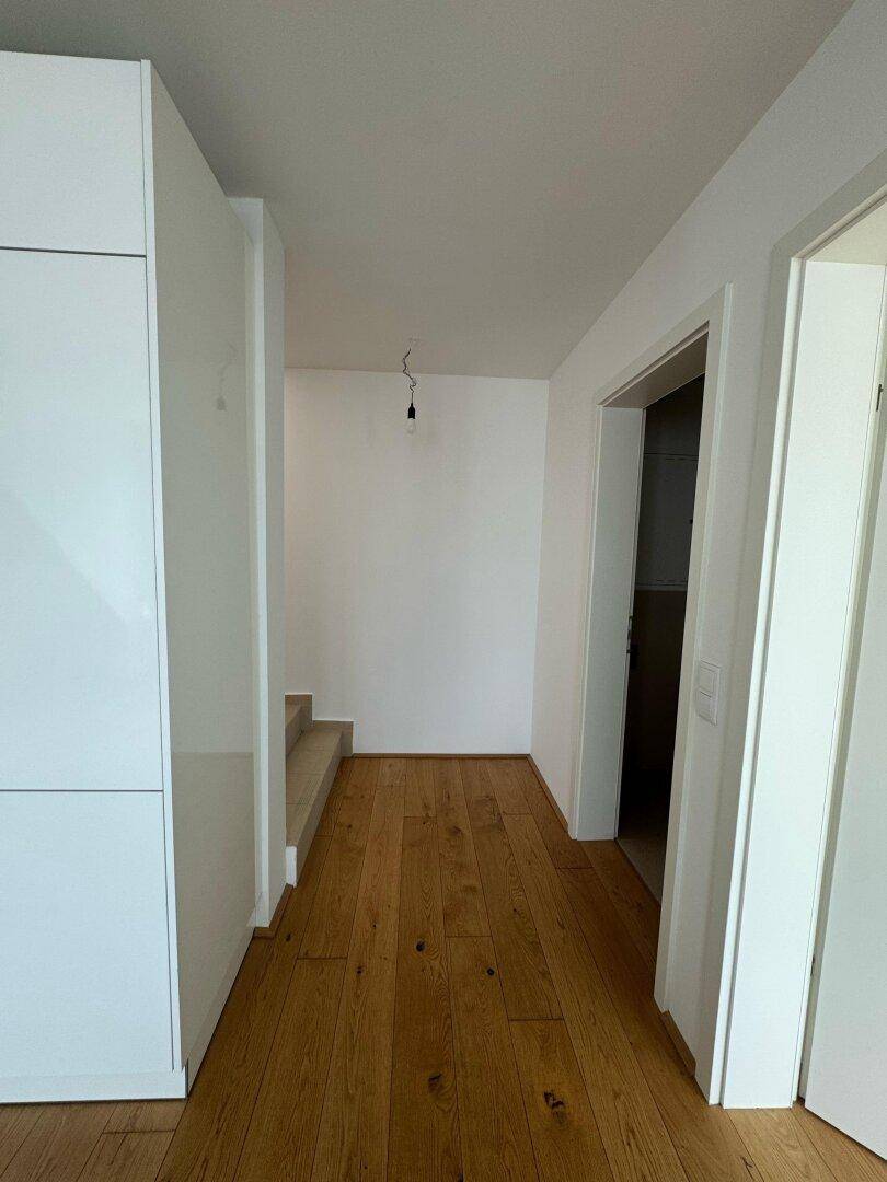 Heller Flur mit Holzboden, weißen Wänden und integriertem Schrank, führt zu einer Treppe.