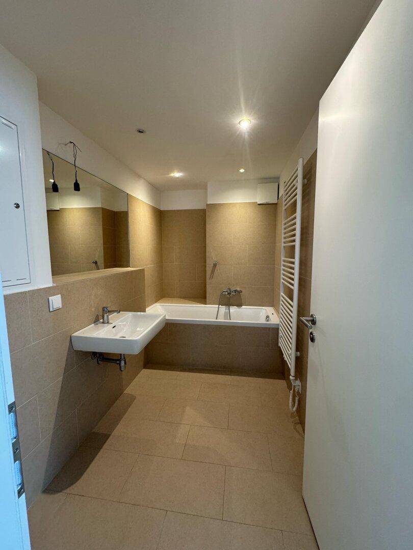 Modernes Badezimmer mit beigefarbenen Fliesen, Badewanne, Einzelwaschbecken und Handtuchheizkörper.