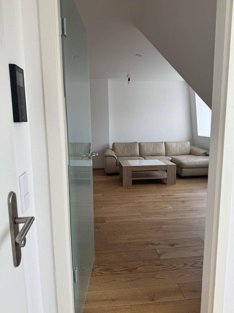 Blick durch eine Tür in den offenen Wohn-Essbereich mit Sofa, Küche und Holzboden.