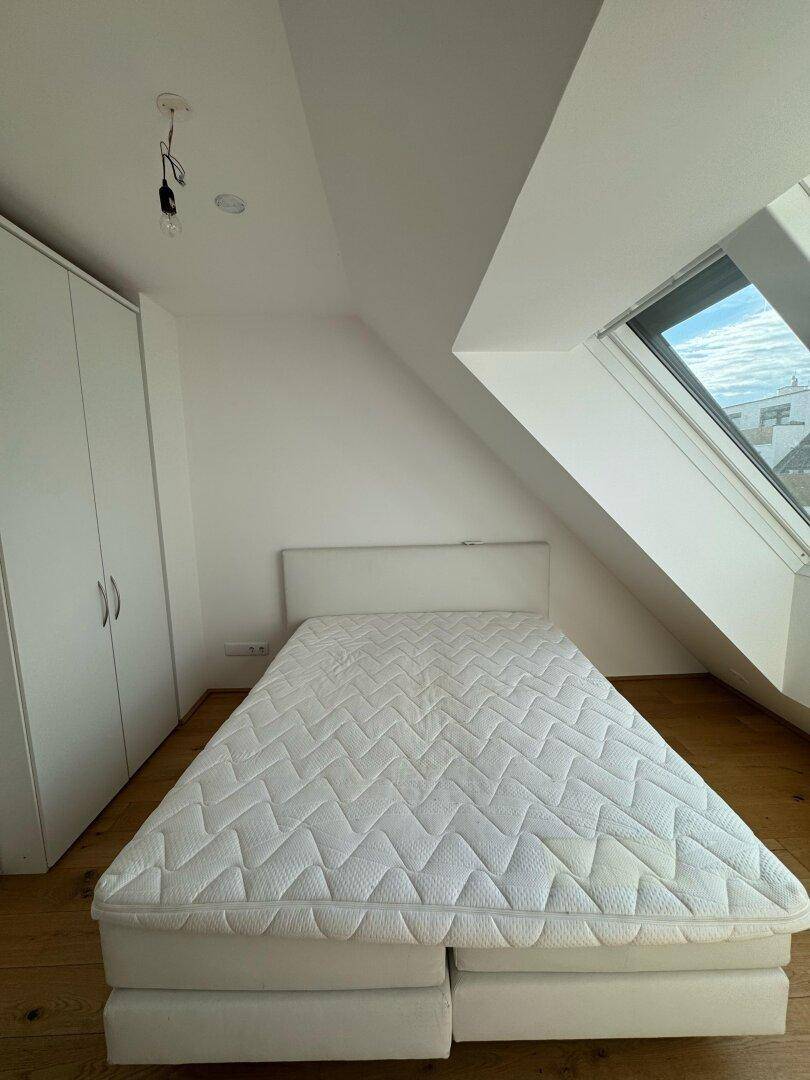 Schlafzimmer mit Bett, weißem Kleiderschrank, Holzboden und großem Dachfenster unter Schrägen.