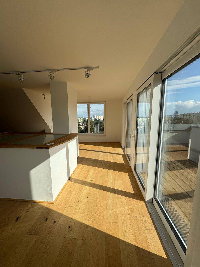 Lichtdurchfluteter Wohnbereich mit Holzboden, großen Schiebetüren zum Balkon und Stadtblick.