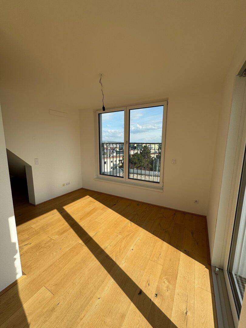 Heller Raum mit Holzboden und großem Fenster, das einen weiten Blick über die Stadt bietet.