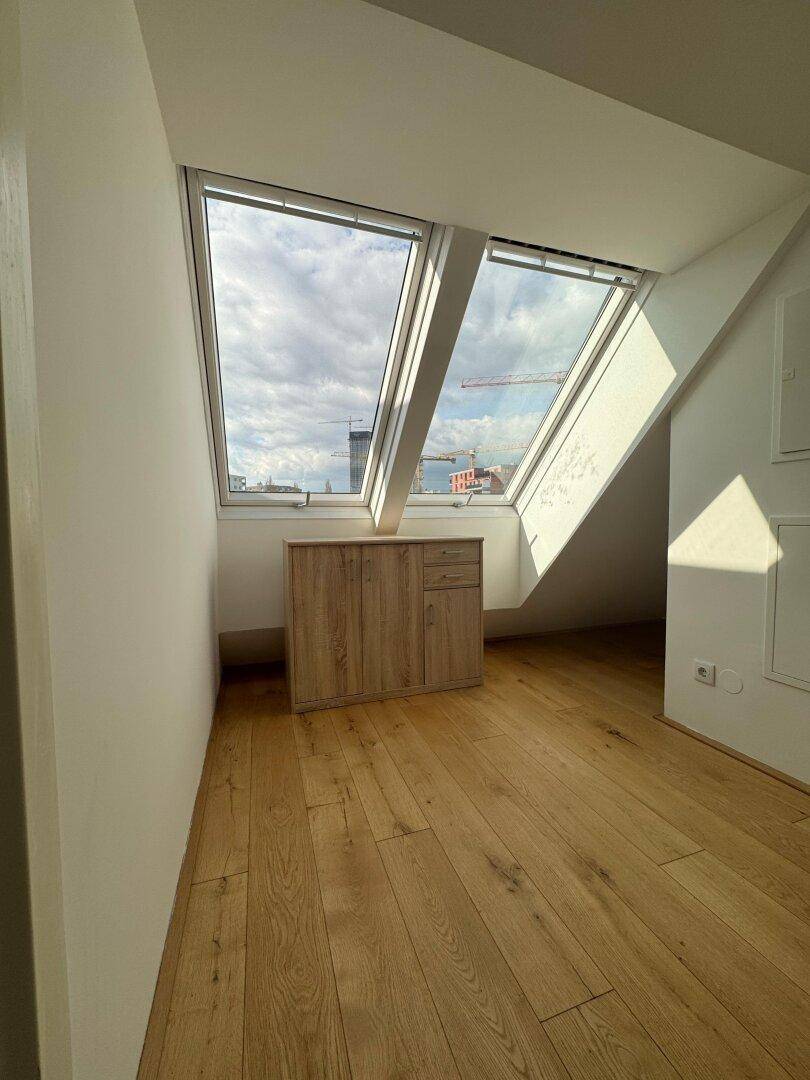 Schlafzimmer mit Holzboden, kleinem Schrank und zwei großen Dachfenstern unter Schrägen.