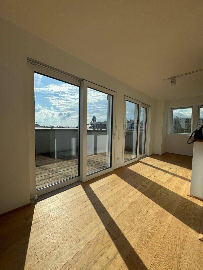 Lichtdurchfluteter Wohnbereich mit Holzboden, großen Schiebetüren zum Balkon und Stadtblick.
