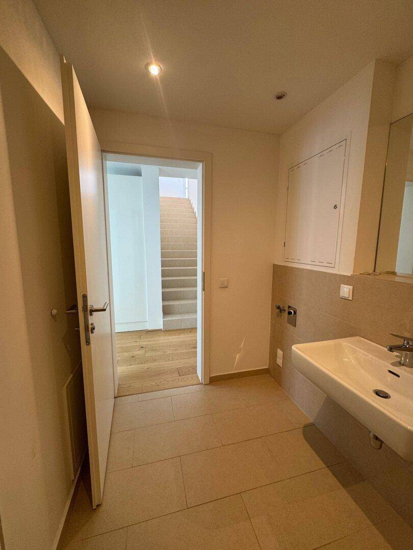 Modernes Badezimmer mit beigefarbenen Fliesen, Einzelwaschbecken und Zugang zum Treppenhaus.