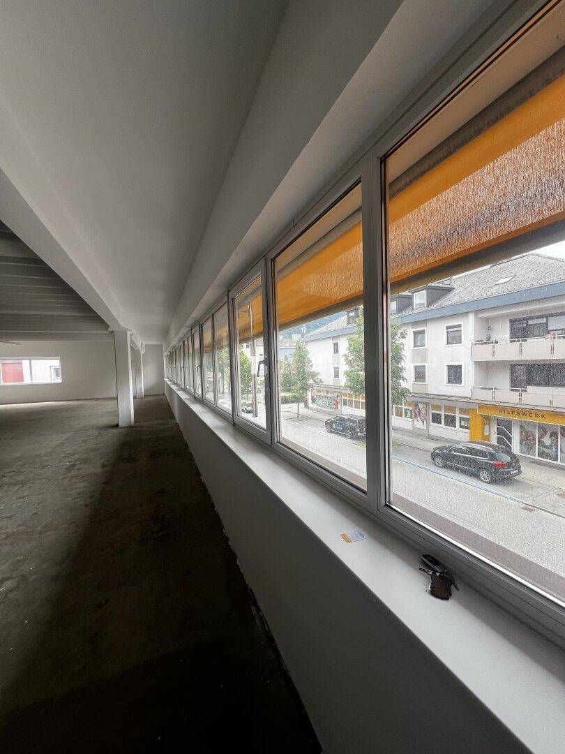 Fensterfront mit Blick auf die Straße und umliegende Gebäude, ausgestattet mit orangefarbenen Rollos.