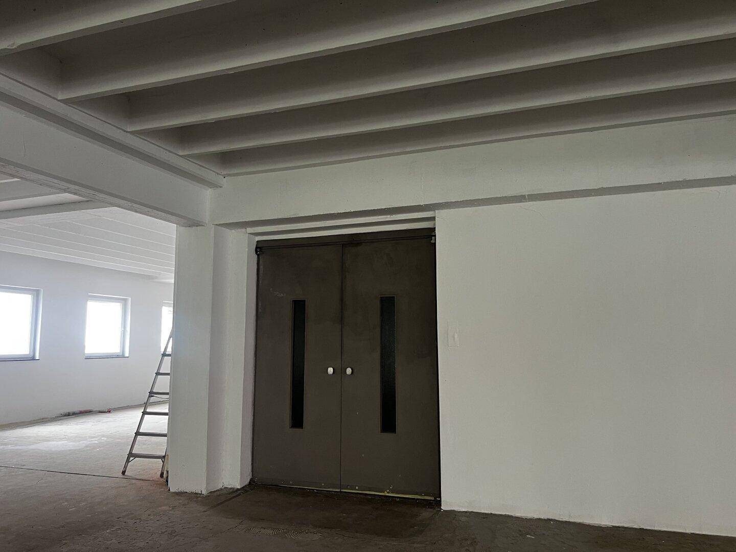 Große Doppeltür in einem Gewerberaum, daneben eine Leiter, die auf weitere Arbeiten hindeutet.