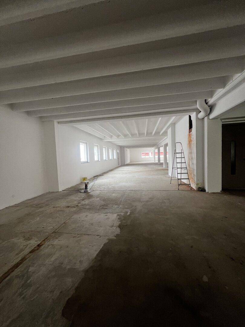 Langer Gewerberaum mit einer Reihe kleinerer Fenster und einer Leiter, die auf die laufende Fertigstellung hindeutet.