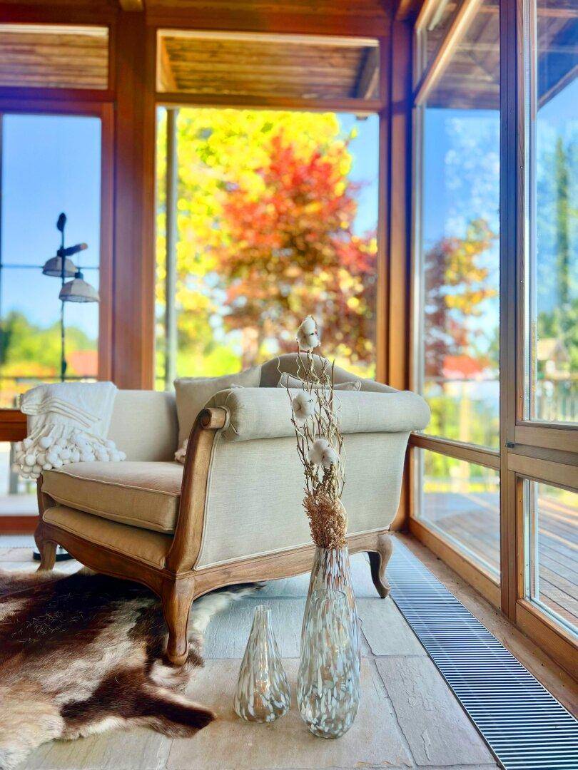 Gemütlicher Wohnbereich mit beigem Sofa, großen Fenstern und Blick auf die herbstliche Natur.