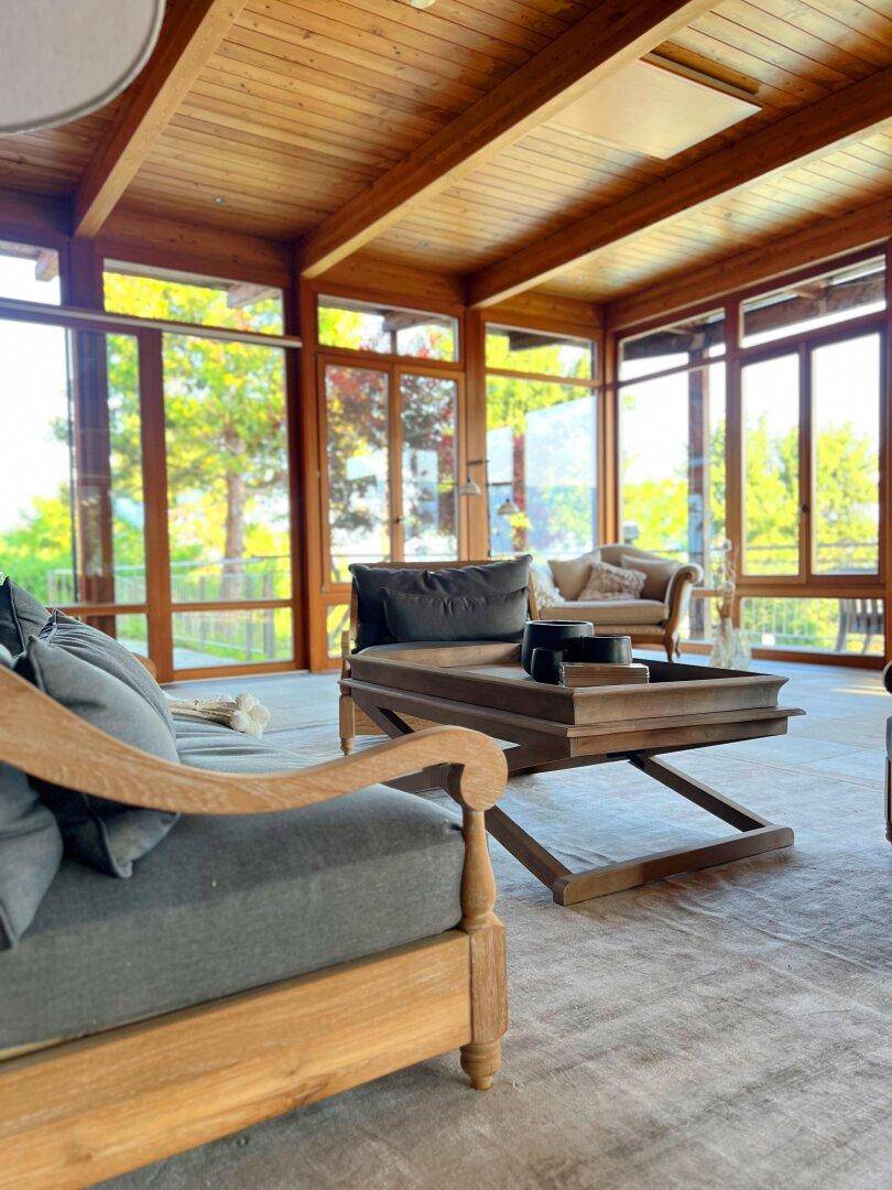 Geräumiger Wohnbereich mit bequemen Sofas, Holzbalkendecke und großen Fenstern mit Blick ins Grüne.