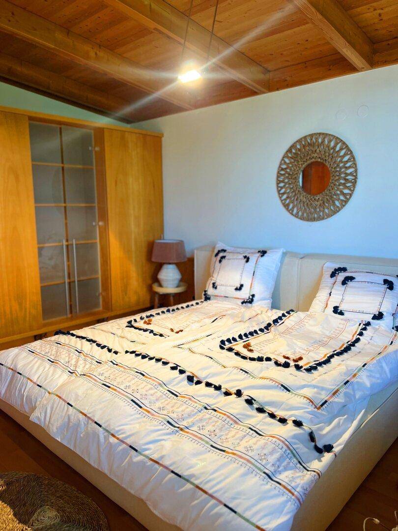 Schlafzimmer mit Holzbalkendecke, Doppelbett und eingebautem Holzschrank, hell und einladend.