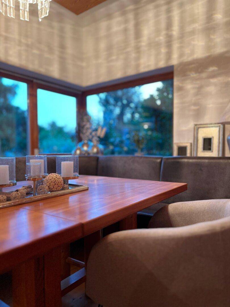 Gemütlicher Essbereich mit Holztisch und großen Fenstern, die viel Tageslicht hereinlassen und Blick ins Grüne bieten.