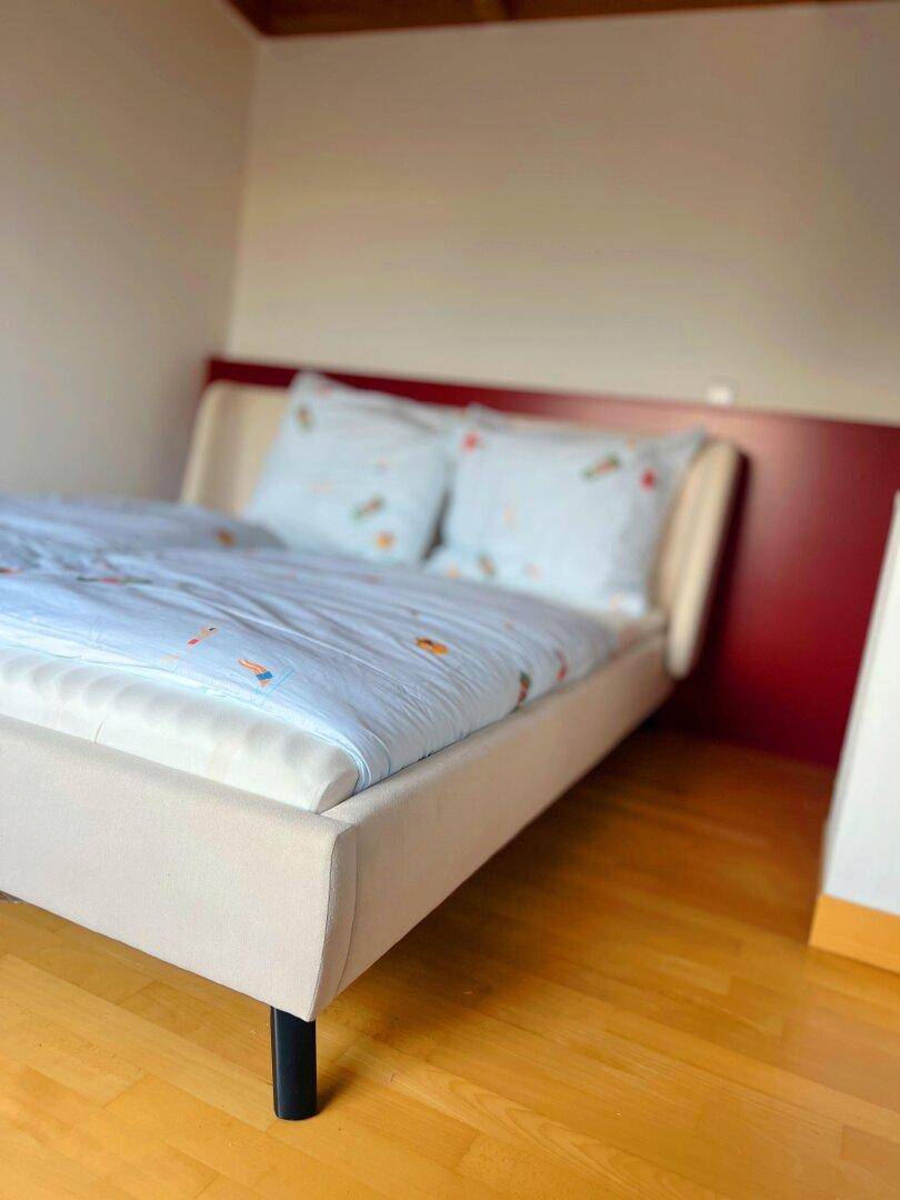 Schlafzimmer mit hellem Holzboden und modernem Bett mit rotem Kopfteil, einfach und funktional.