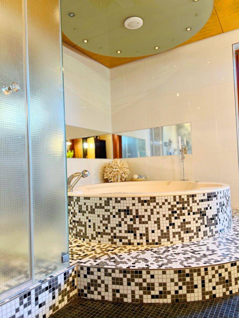 Modernes Badezimmer mit runder, gefliester Badewanne und separater Glasdusche.
