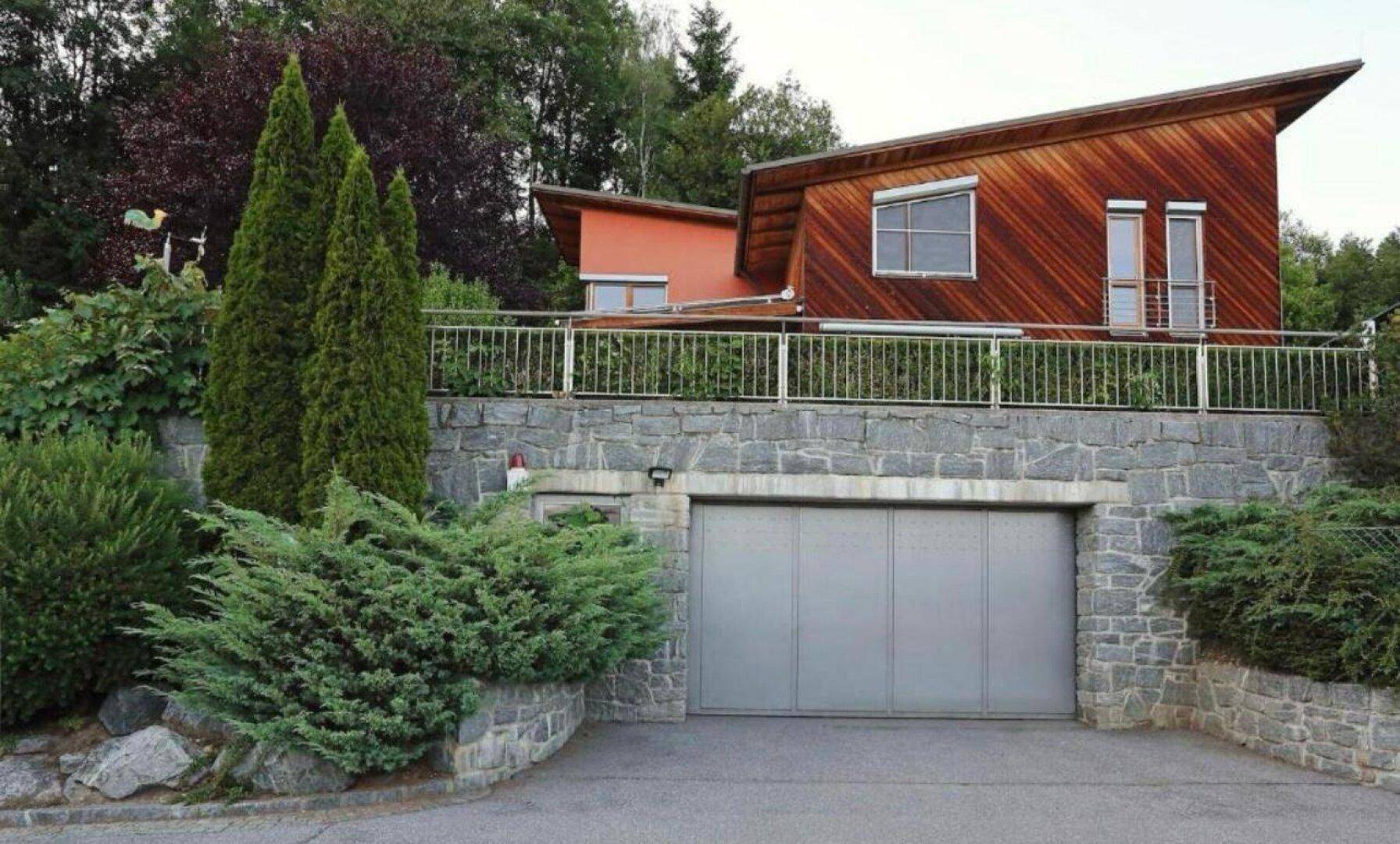 Modernes Haus mit Holzfassade, schrägem Dach und integrierter Garage in einer Steinmauer.