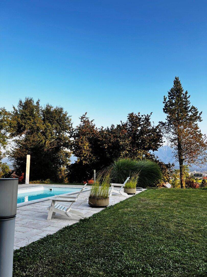 Gepflegter Gartenbereich mit Swimmingpool, Liegestühlen und weitem Blick auf die Berge.