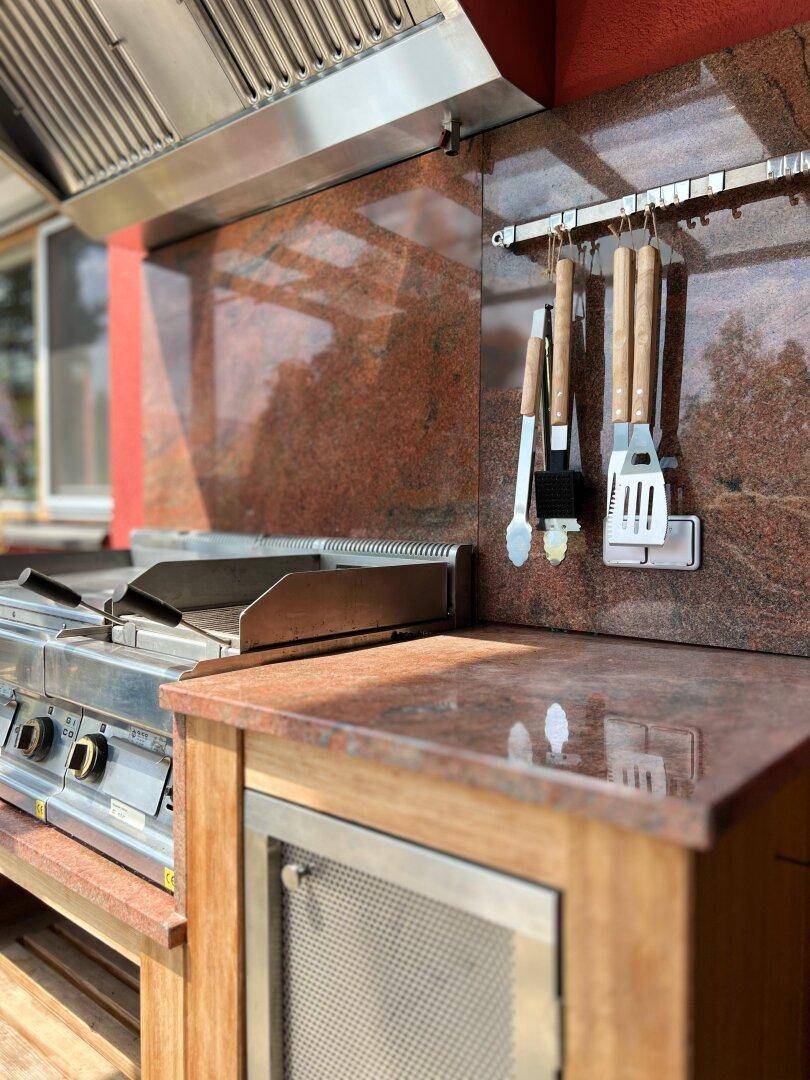 Exklusive Außenküche mit Edelstahlgrill, Granitarbeitsplatten und Holzschränken.