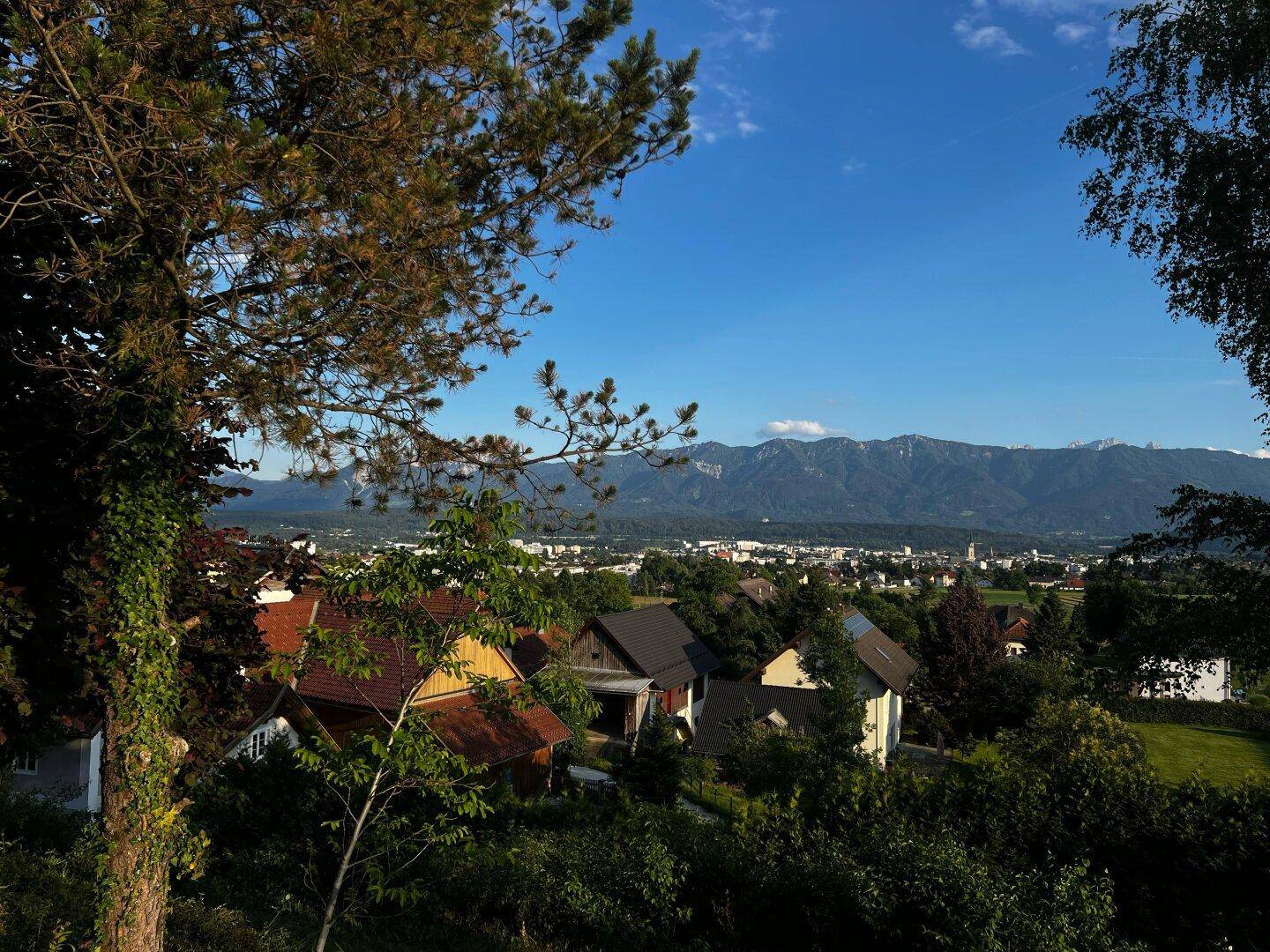 Malerischer Ausblick auf eine Stadt mit Bergen im Hintergrund, umgeben von üppigem Grün.