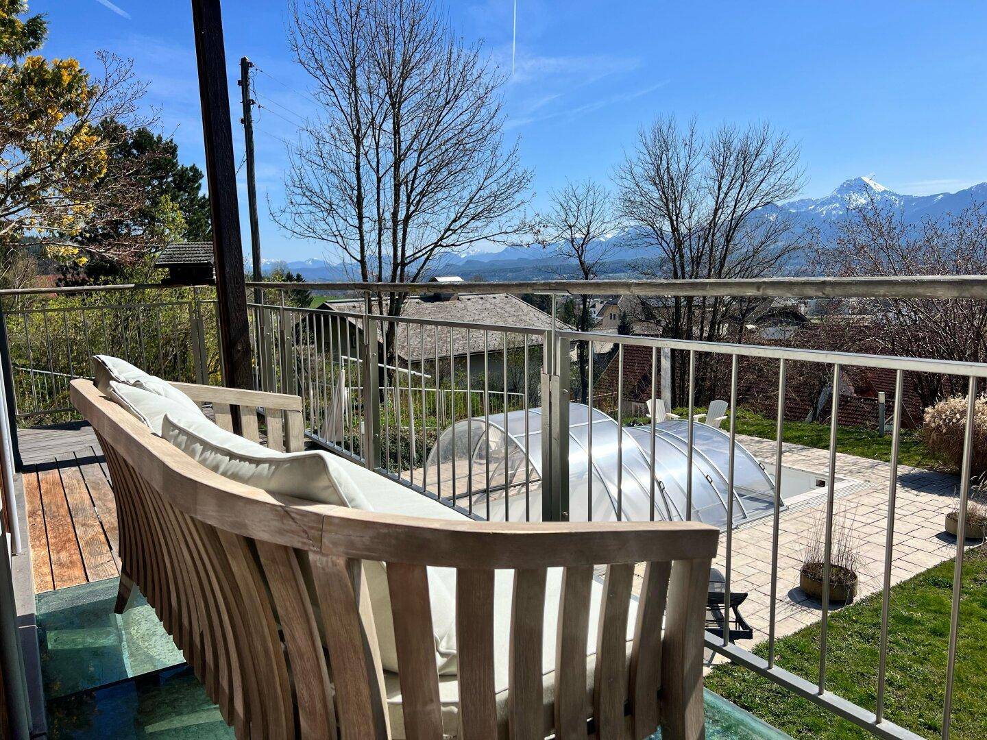 Balkon mit Holzbank, Metallgeländer und Panoramablick auf die Berge und den Poolbereich.