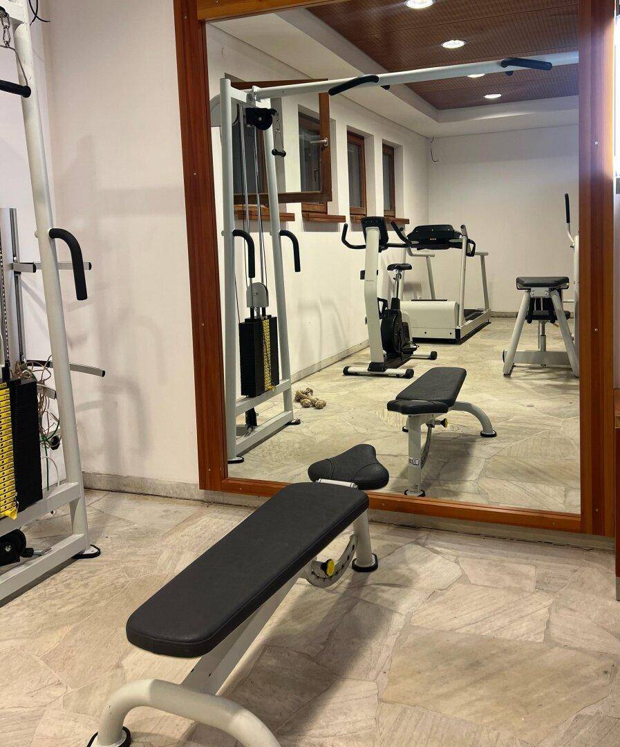 Gut ausgestatteter Fitnessraum mit verschiedenen Trainingsgeräten und großem Wandspiegel.