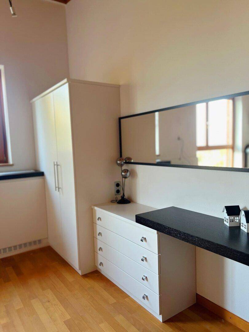 Helles Schlafzimmer mit weißem Kleiderschrank, Kommode und großem Wandspiegel.