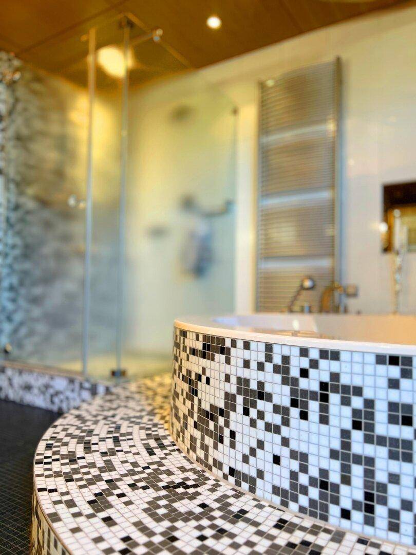 Modernes Badezimmer mit gefliester Badewanne, Glasdusche und beheiztem Handtuchhalter.