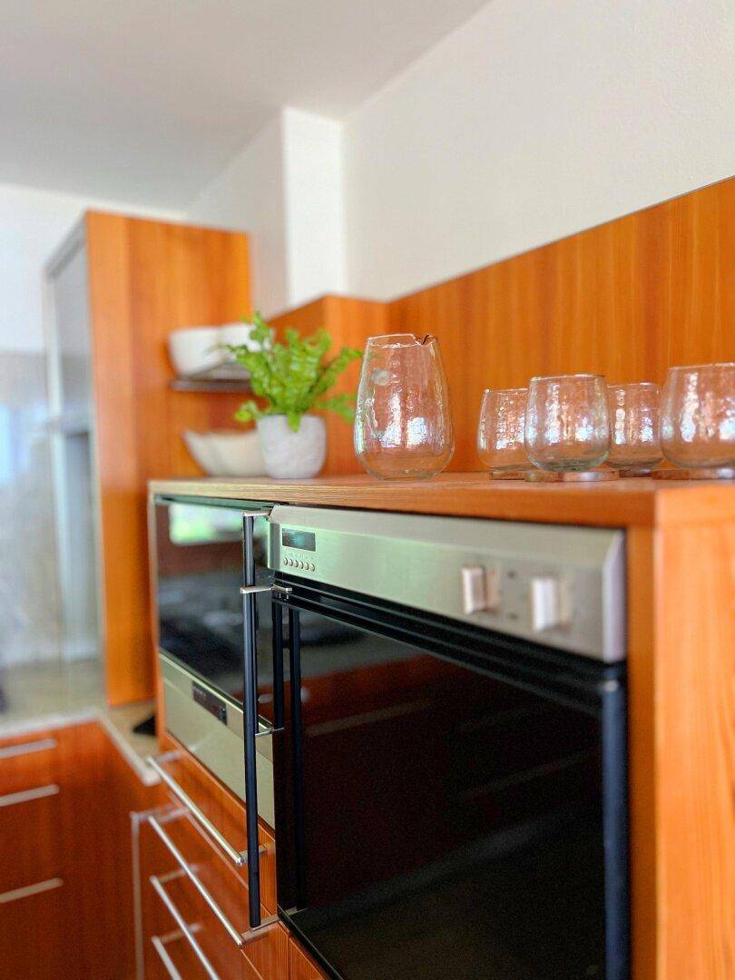 Eingebaute Backöfen und Mikrowelle in einer modernen Holzküche mit Ablageflächen.