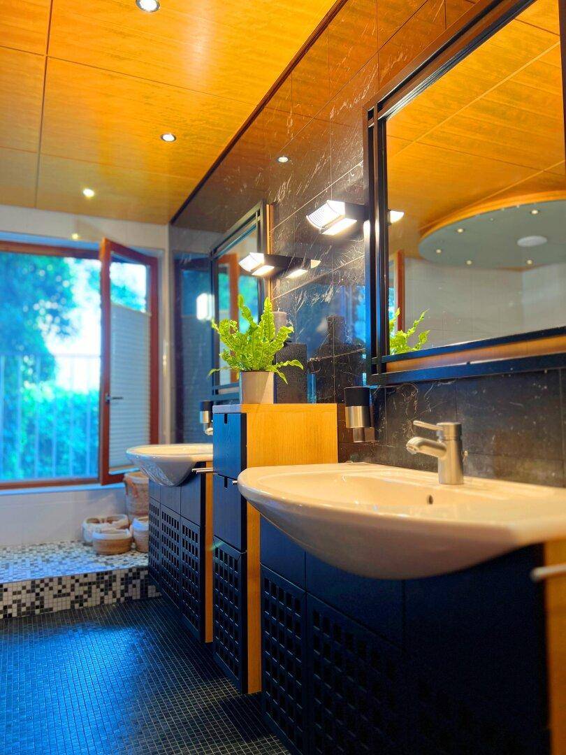 Modernes Badezimmer mit zwei Waschbecken, dunklen Fliesen und großem Fenster.