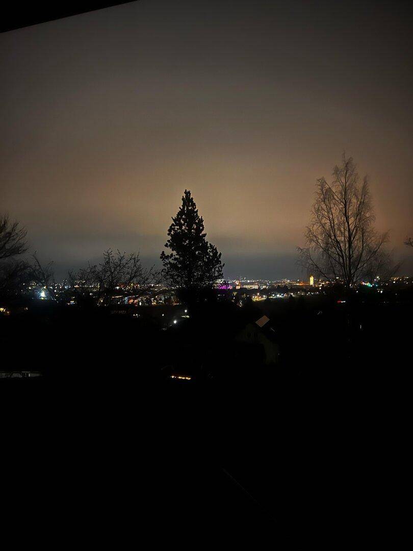 Nächtlicher Panoramablick auf die beleuchtete Stadtlandschaft unter einem dunklen Himmel.