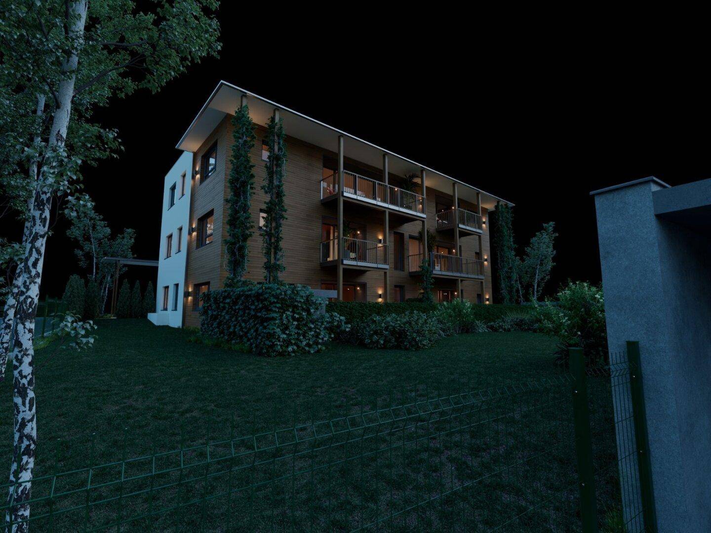 Nachtaufnahme der modernen Wohnanlage mit Holzfassade, Balkonen und gepflegter Hecke im Vordergrund.