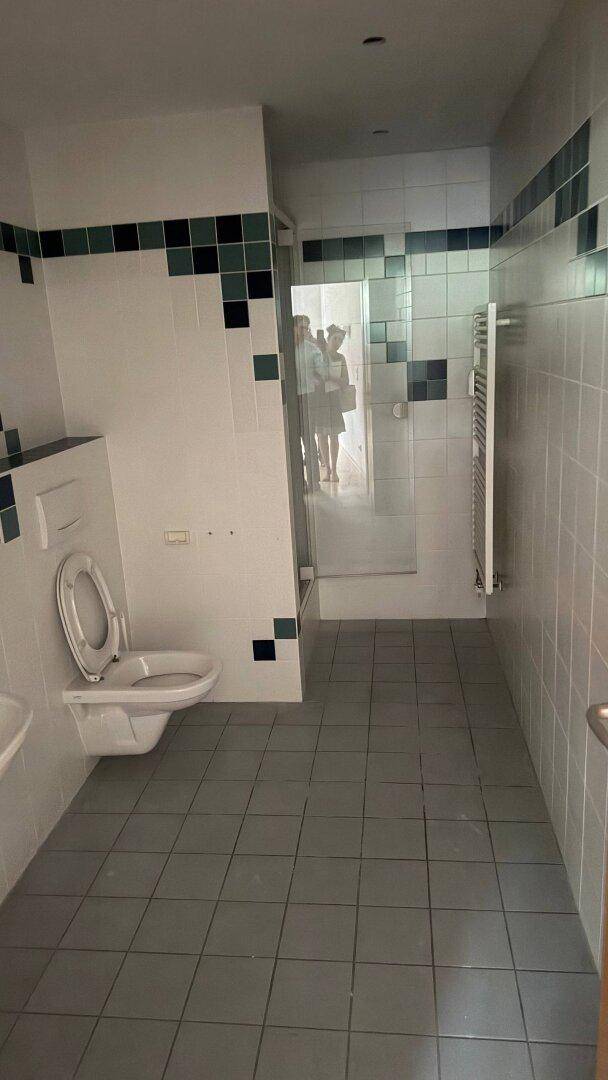 Badezimmer mit gefliesten Wänden in Weiß und Dunkelgrün, einer Toilette und einem Heizkörper.