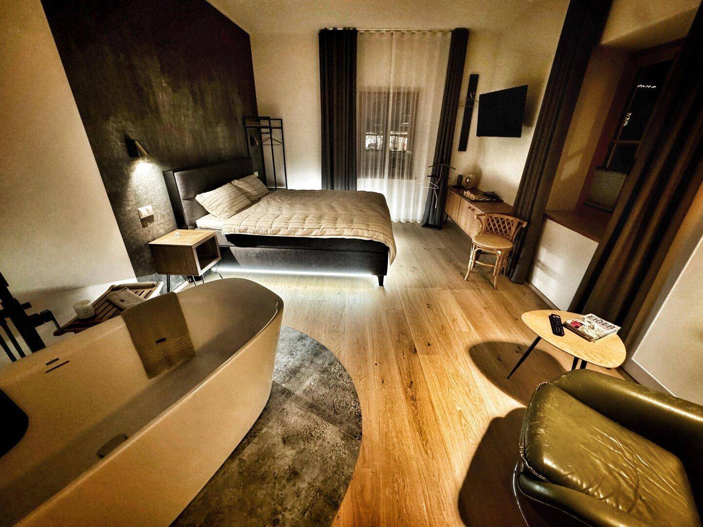 Modernes Schlafzimmer mit Holzboden, dunklen Wänden und einer freistehenden Badewanne im Raum für luxuriöses Wohnen.