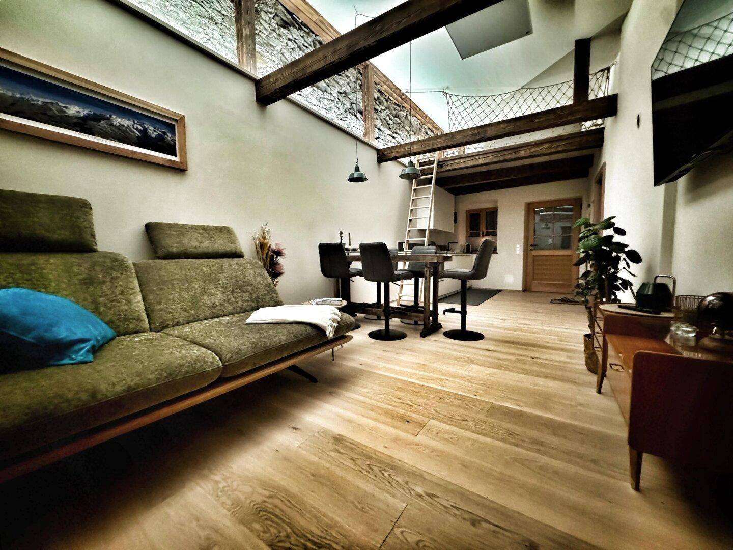 Offener Wohn-Essbereich im Loft-Stil mit Holzboden, freiliegenden Holzbalken und einer markanten Steinwand.